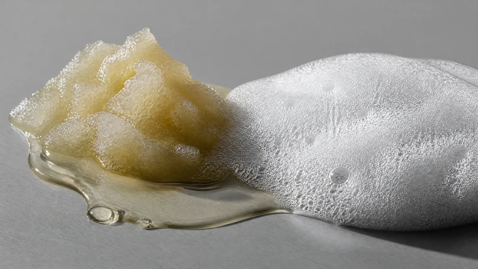 A scoop of sherbet cleansing balm melting into clear oil beside a mound of dense white cleanser foam