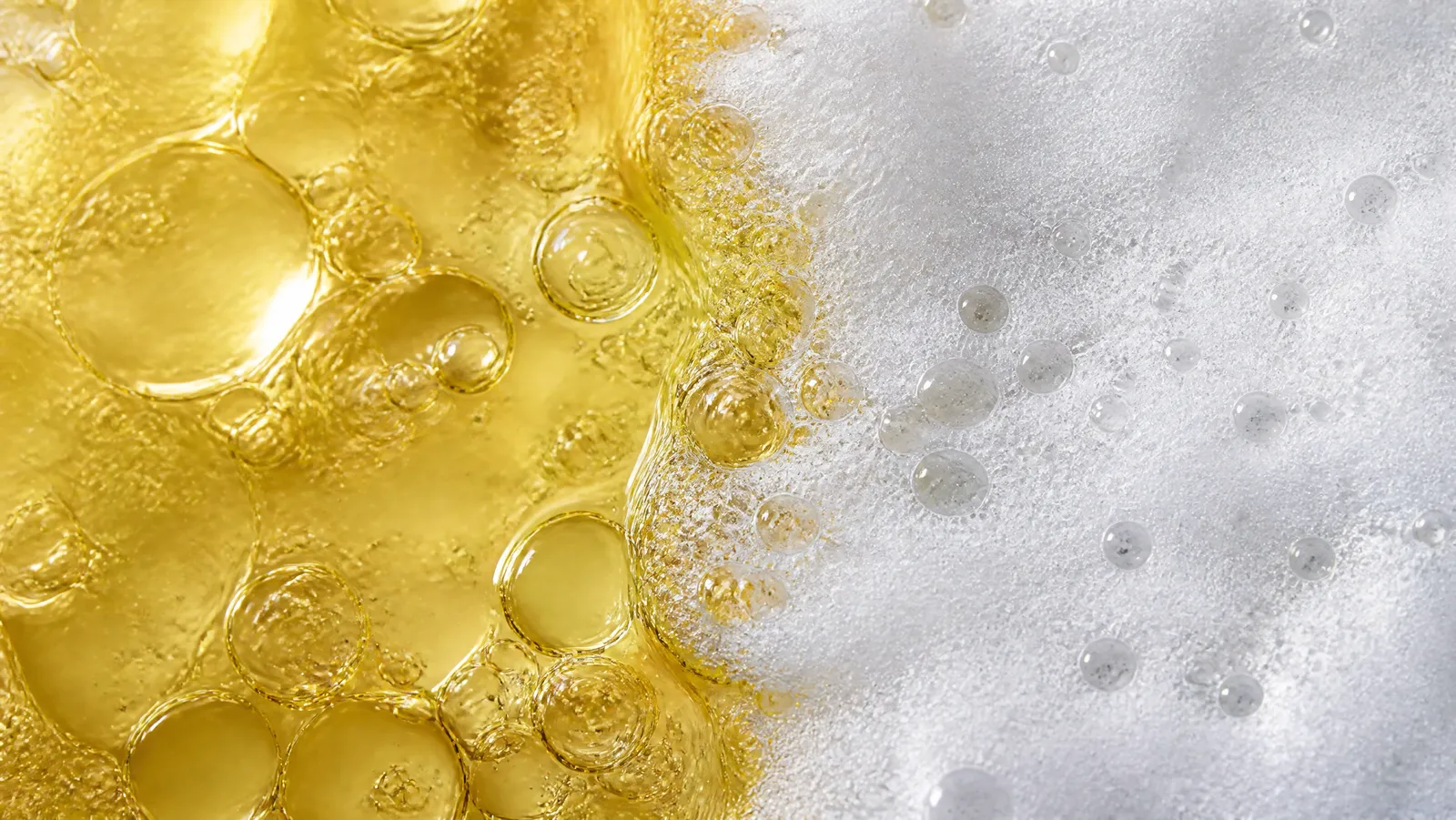 Golden cleansing oil beading against dense white cleansing foam along a vertical boundary
