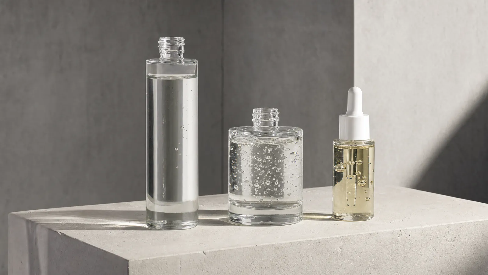 Three unbranded glass bottles showing the differing viscosities of an essence, a serum and an ampoule
