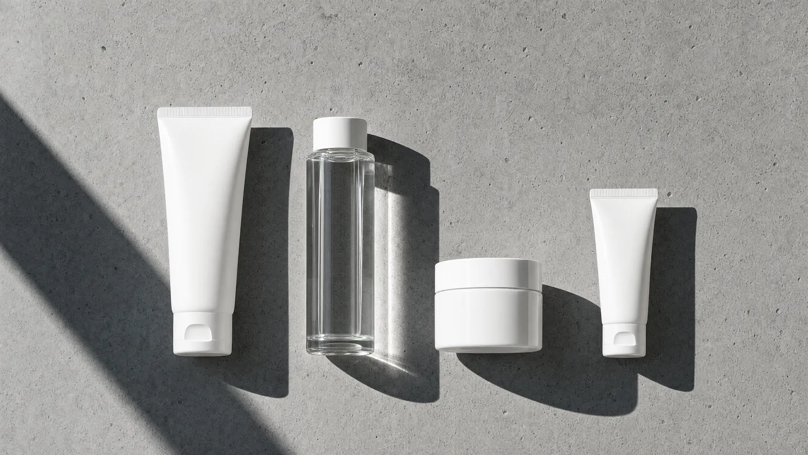 Overhead flat lay of a four-step Korean skincare starter set on grey concrete in hard daylight