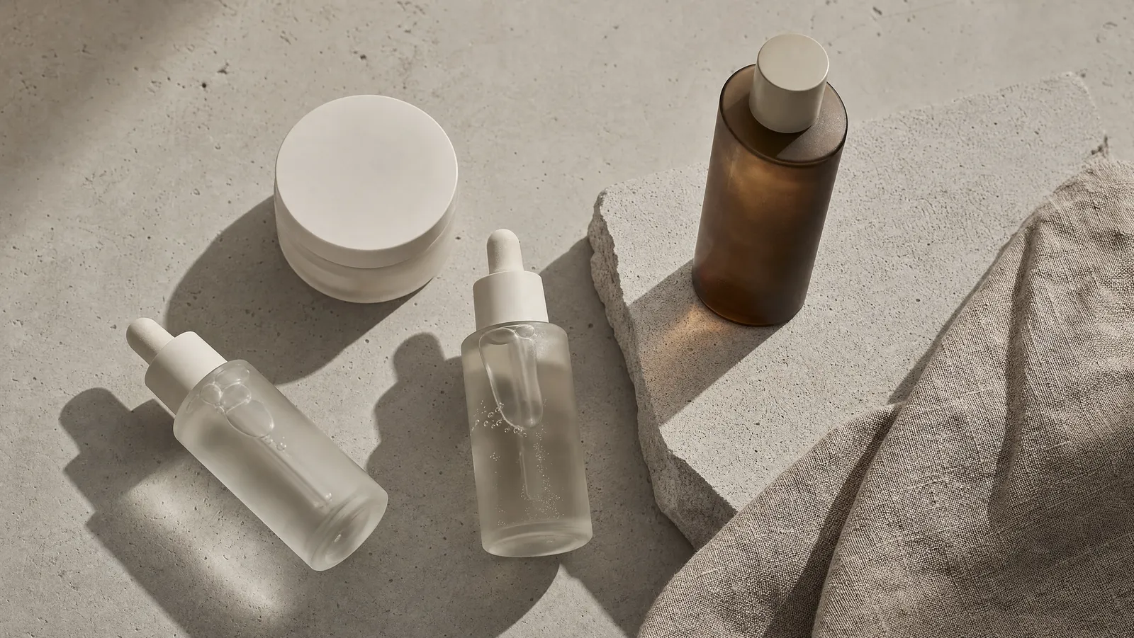 A minimalist flat lay of Korean skincare bottles and jars on a concrete surface